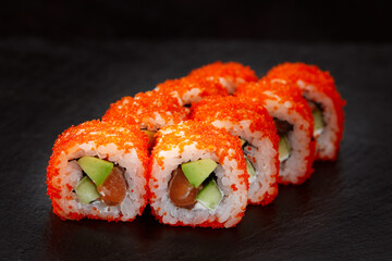 appetizing sushi roll california with avocado shrimp cheese and masago caviar on a black background.
