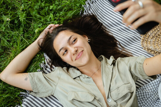 top view of laughing brunette woman lying on grass in park
