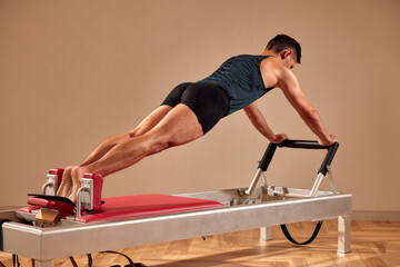 Side view of barefoot male athlete lying on pilates reformer and performing abs exercise during...