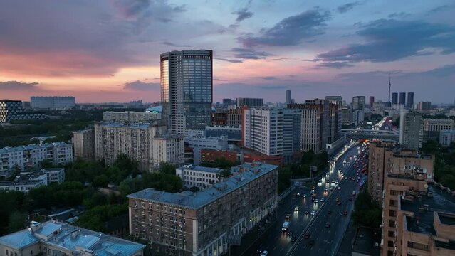 Aerial view of a beautiful sunset over the streets of Moscow in pink and red colors against a cloudy sky. The roofs of houses and the movement of cars on the roads.