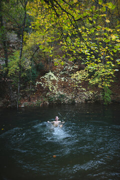 Young man swimming in river in autumn forest