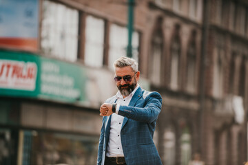 Fototapeta premium Senior businessman walking in the city, carrying a bag and using a watch