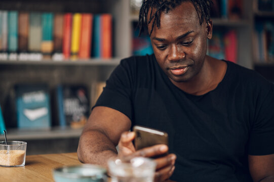African american man using smartphone while drinking coffee in a cafe - Powered by Adobe