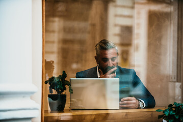 Modern senior businessman sitting in cafe and using laptop and smartphone