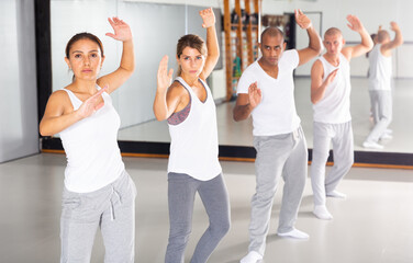 Group of beginners mastering martial arts for self defence, synchronously repeating basic movements in gym..