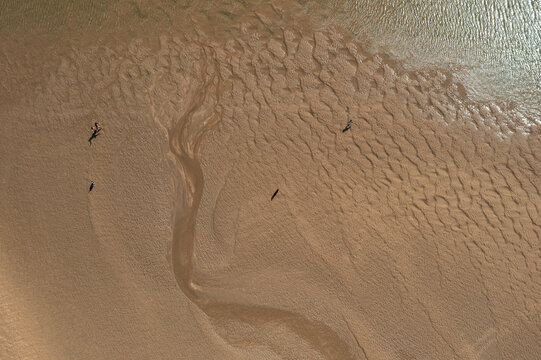 aerial image of people walking on a  wet beach during low tide