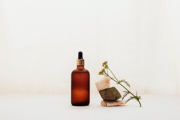 Brown cosmetic oil or serum bottle and yarrow flower on white background. Natural cosmetics, spa and wellness concept