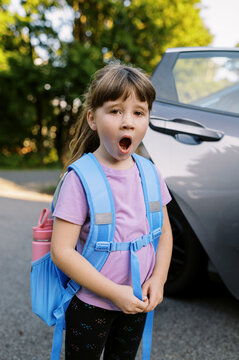 little school girl with backpack on, yawning by the car 