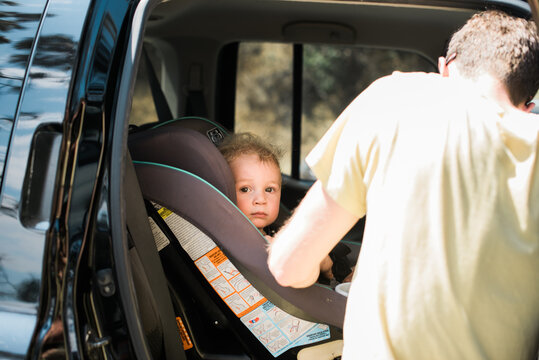 Young father strapping his son into the backseat of his SUV
