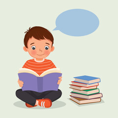 Cute little boy reading a book sitting on the floor beside stack of books