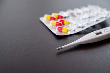 White thermometer on a dark table with a carton of colored pills. Fever concept. Medicine concept.