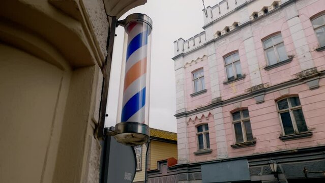 Red white and blue barbershop pole is spinning in an old town against windows and sky
