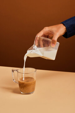 Crop female pouring milk into coffee