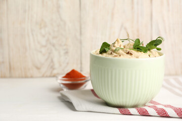 Bowl of tasty hummus with pea leaves on white wooden table, space for text