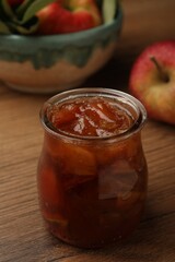 Tasty apple jam in glass jar on wooden table, closeup