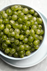 Bowl full of ripe gooseberries on light grey marble table, top view