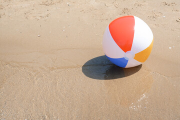 Obraz premium Colorful beach ball on wet sand at seaside, space for text