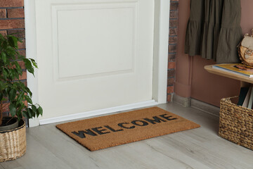 Door mat with word Welcome on wooden floor in hall - obrazy, fototapety, plakaty