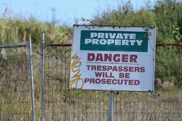 Private Property Danger Trespassers will be Prosecuted sign attached to gate overgrown grass bush...