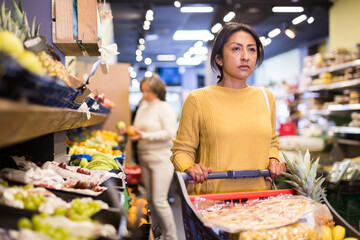 Positive woman choosing food products on shelves in grocery shop