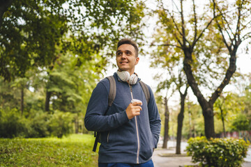 One young adult caucasian man walking in the city or town near park with cup of coffee in autumn or spring day happy male tourist standing alone real people copy space