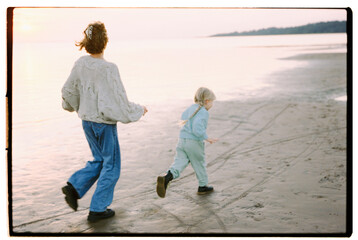 Obraz premium BACK VIEW: Little daughter runs with his mother on a beach