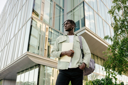 Student standing near campus carrying notebooks