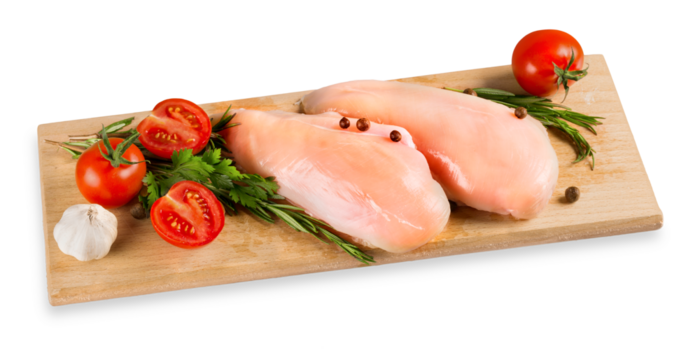 Raw turkey breasts with vegetables, spice and herbs on wooden cutting boardRaw turkey breast with tomatoes and garlic on cutting board