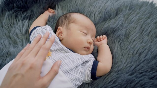 0-1 month Asian newborn boy sleep on blue cotton fur happy and tender, mother hand put on infant's chest to protect or prevent flinch or appalled while toddler sleeping, hospitality motherhood concept