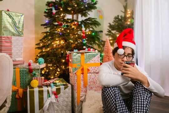 Teen boy using the phone by Christmas tree