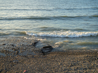 Coastline. Waves gently roll on the shore. Pebble and black sand beach. Big boulder.