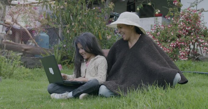 Slow-motion shot of a grandmother and granddaughter sitting outside using the laptop