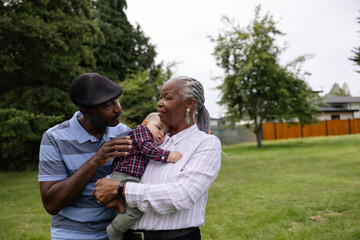 Grandparents holding baby grandson outside in park.