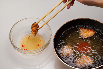 揚げたての素揚げした鶏肉をピリ辛のタレに漬け込む　調理中の写真
