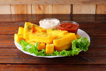 Fried polenta sticks in white ceramic plate over rustic wooden table