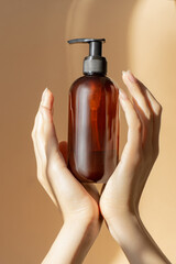 Amber bottle, with dispenser, sprayer, for liquid soap, shampoo, lotion in sunlight. Women's hands...
