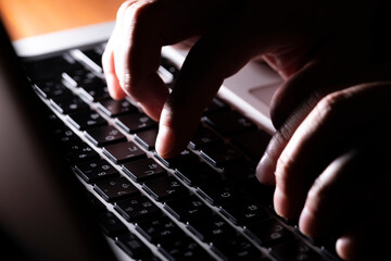 暗い部屋でパソコンを操作してキーボードで入力作業している男性の手