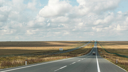 On the vast grassland, a highway stretches into the horizon.