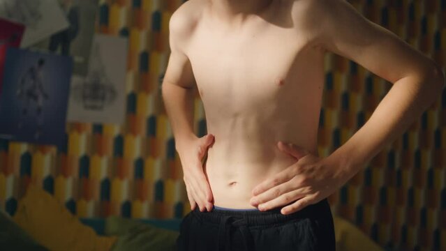 Determined blonde boy looks at his abs in front of the mirror in his room after exercise. Planning to get six packs. Shirtless boy checks progress and training results. Athelete young boy.