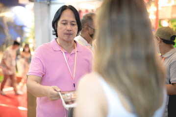 A male visitor at an expo receives a brochure from a sales representative at one of the booths.