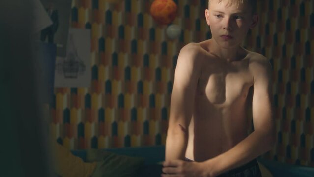 Young shirtless boy looks at his abs in front of the mirror in his room after exercise. Checks progress and training results. Bruised arms. Athelete young boy.