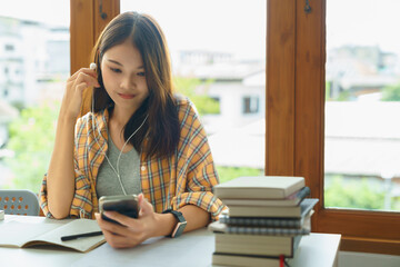 Education and literacy concept, College girl is listening music on smartphone after reading book