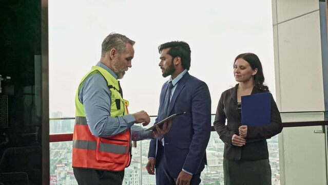 White caucasian professional construction architect holding an architecture plan discussing the project agreement with his client an asian businessman on a digital tablet while his secretary watching
