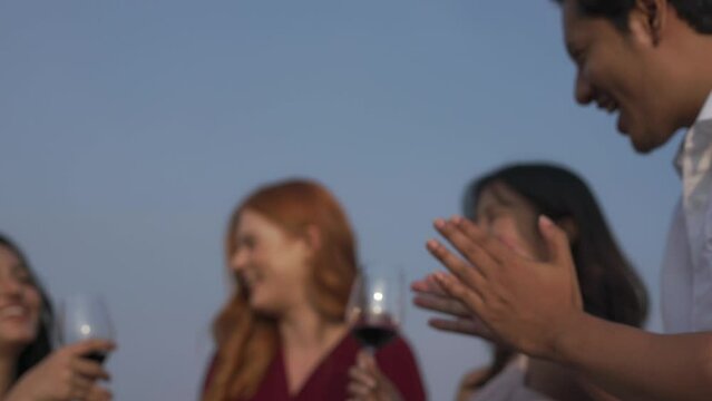 Group of friends of western and asian male and females lady having good time drinking wine in a rooftop bar in the city of Bangkok while touring the site as tourists during a sunset time
