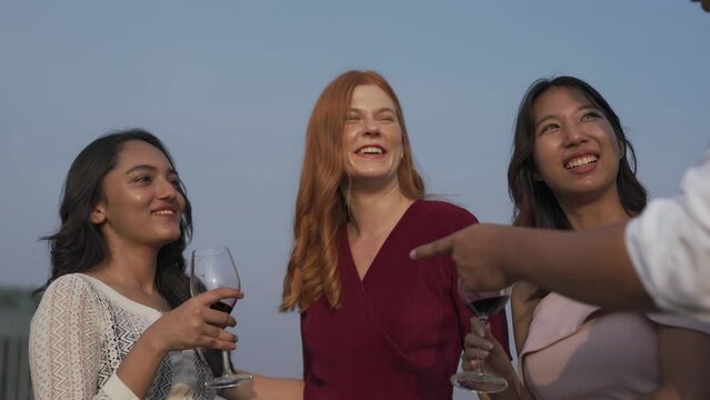 Group of friends of western and asian male and females lady cheering talking chit chat to each other and in a rooftop bar in the city of Bangkok while touring the site as tourists during a sunset time