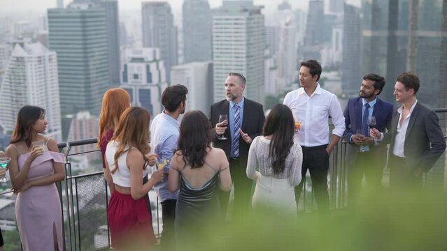 Group of businessmen and businesswomen mingle with each other drinking wine and champagne on a rooftop bar celebrating the successful of company latest deal and hit target goal of the year