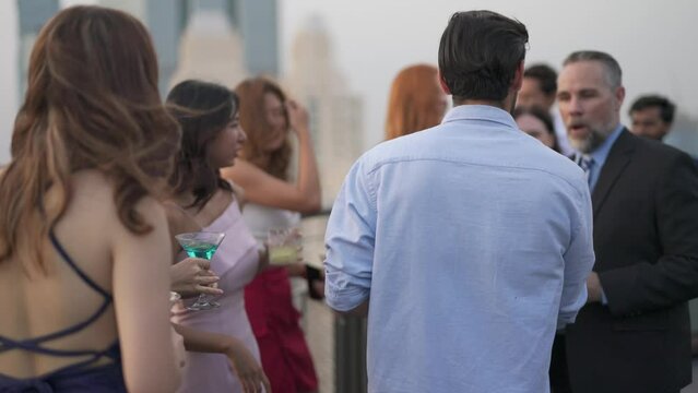 Group of businessmen and businesswomen mingle with each other drinking wine and champagne on a rooftop bar celebrating the successful of company latest deal and hit target goal of the year