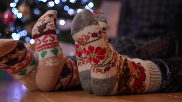 Side view close-up feet in socks with Christmas print moving on wooden parquette floor in living room. Unrecognizable couple sitting at home on New Year's eve resting enjoying leisure