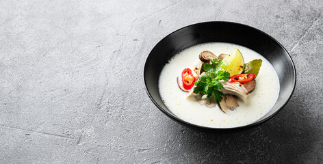 Tom Kha Gai, Thai Galangal chicken coconut soup in a black bowl on a concrete background, copy space