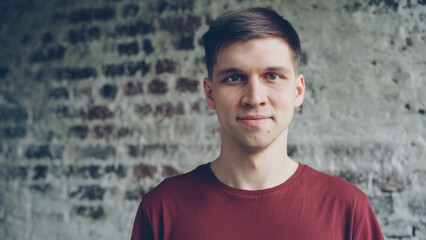 Close-up portrait of dark-haired handsome young man in bright T-shirt smiling and looking at camera. Young happy people, loft style interior and happiness concept.